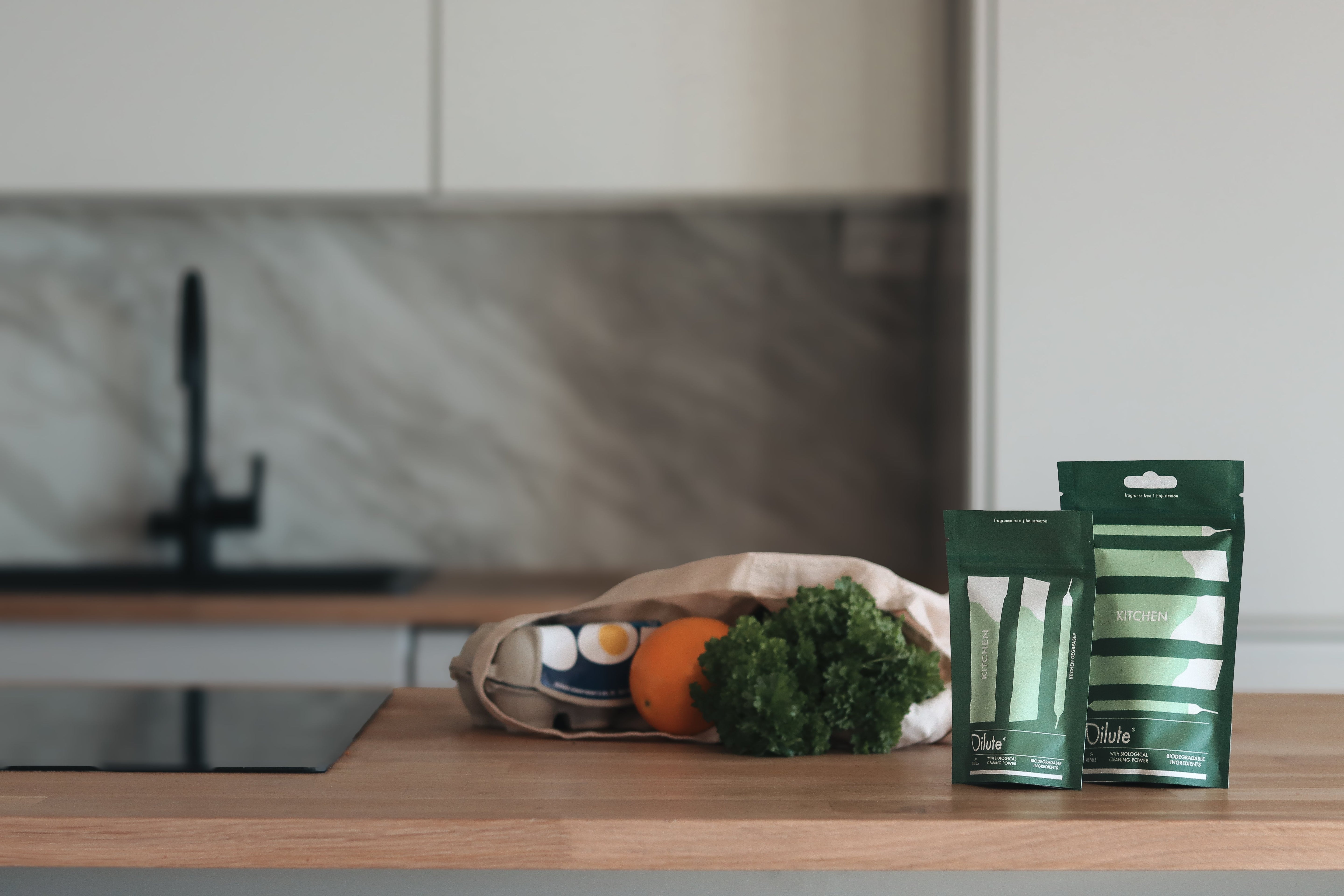 Ekologiset puhdistusaine refill-paketit keittiössä vihannesten rinnalla, minimalistinen ja luonnollinen sommittelu