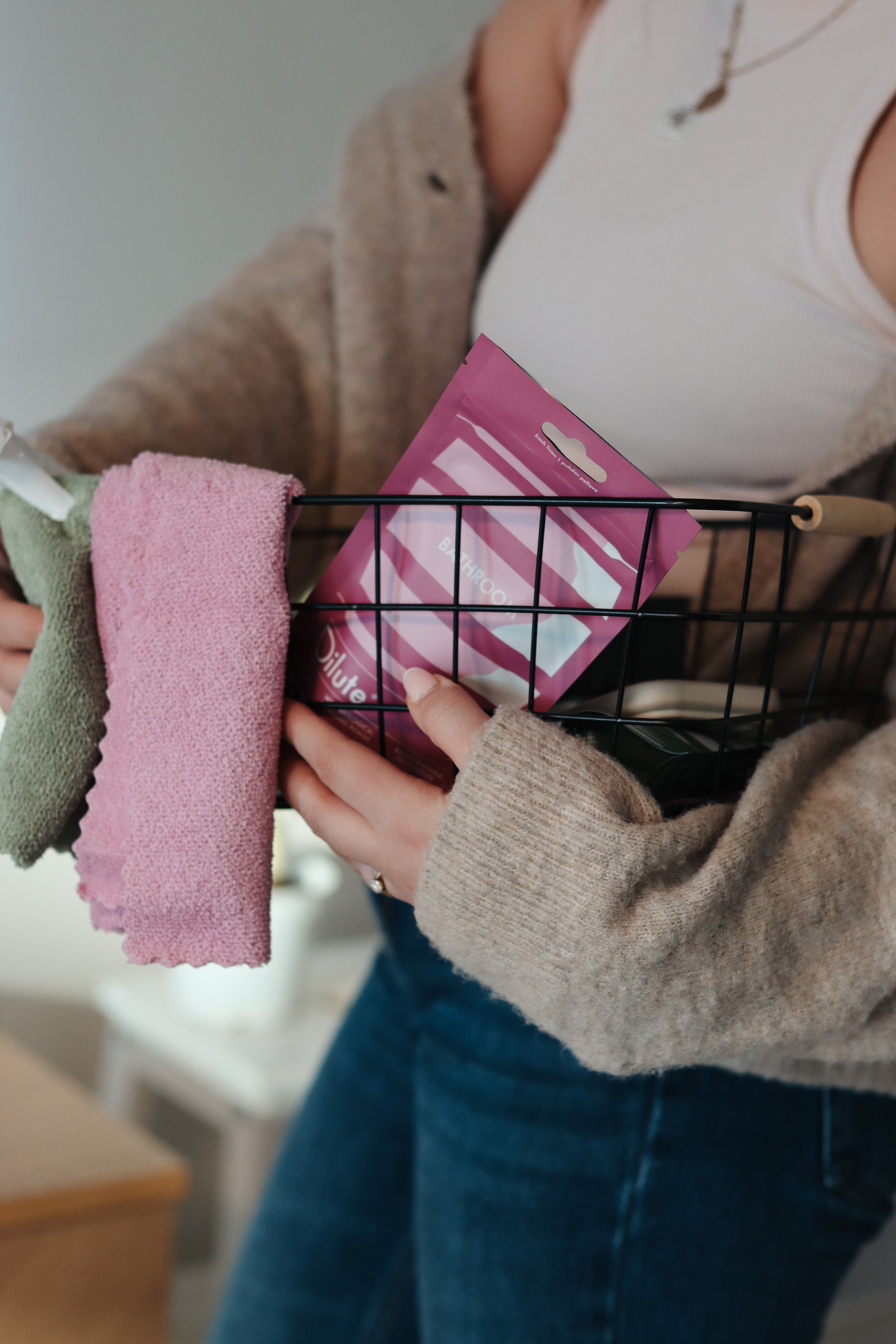 Nainen pitää koriin asetettuja pyyhkeitä ja "Dilute Bathroom" -tuotepakkausta.